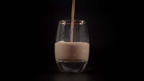 Pouring chocolate milk shake into empty glass. Close up on luxury glass filled with chocolate milk on dark background.