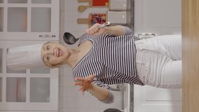 Housewife wearing chef hat sings with ladle and dances in the kitchen. Young woman having fun alone. The concept of having fun alone.Video for the vertical story.