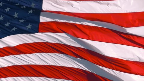 Close up slow motion footage of USA flag waving in the wind on a bright sunny day. Moving and amazing slow motion closeup of American Flag gracefully waving in wind. Close up of American flag waving.