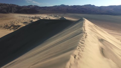 Drone flying fast revealing desert mountain panorama. Cinematic massive dunes hills in golden soft light. Aerial fast b roll shot of sand dune peak with desert wilderness on background at sunset, 4K