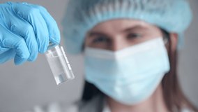 Close-up of a woman holding a test tube with a vaccine. GP wearing medical mask in a laboratory. High quality 4k footage