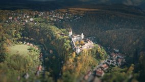 An aerial view of the Krivoklat Castle in Czechia. A beautiful medieval castle towering above the valley. Forest covering nearby hills. Small villages scattered in-between. A tilt-shift video.