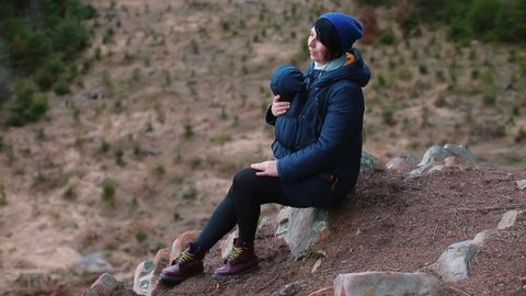 Woman in sling jacket spends time in mountains with child. Relaxation in fresh air. Invisible connection between mother and child. Relaxation of young parent baby sling jacket.