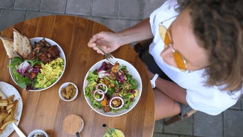 Top view of a female eating a salad served on the wooden table