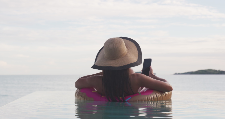 5G phone fast internet connection on Vacation woman on inflatable donut float using mobile cell phone in swimming pool. Girl relaxing relaxing enjoying travel holidays at resort pool in bikini. Royalty-Free Stock Footage #1070722393