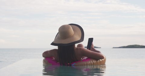 5G phone fast internet connection on Vacation woman on inflatable donut float using mobile cell phone in swimming pool. Girl relaxing relaxing enjoying travel holidays at resort pool in bikini.