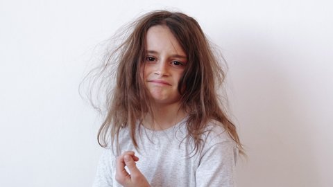 Child haircare. Beauty care. Hygiene cosmetology. Dissatisfied disappointed unhappy little girl with dry tousled tangled untidy messy hair isolated on light background.
