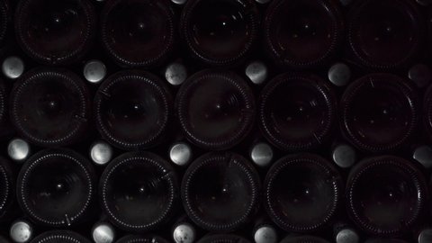 Close up shot of Wine bottles lying in stack at cellar. Glass bottles of red wine stored in wooden shelving in stone cellar. Interior underground wine cellar in winery