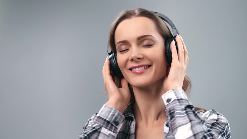 Closeup face of pretty young feminine laughing dental smile enjoying pleasant audio sound. Cheerful lady in headphones listen music at disco party isolated on gray. Shot on RED Raven 4k Cinema Camera