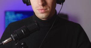 Close-up of male blogger in headphones talking in microphone recording podcast in studio