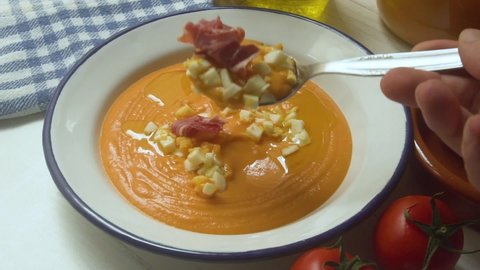 Eating Traditional tapa Salmorejo from south Spain. Cold tomato soup with ham, egg and olive oil.