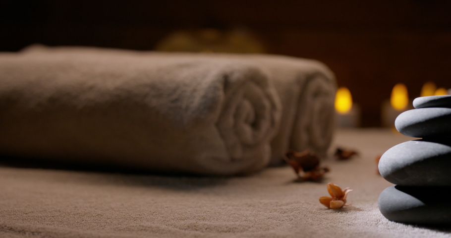Spa salon equipment. Close up shot of massage hot stones with little flowers around and towels with flaming candles on background - wellness, spa concept 4k footage Royalty-Free Stock Footage #1070735809