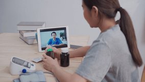 Asian young adult female patient video call with male doctor discussing for medicine and pill. New normal online medication pharmacy at home concept