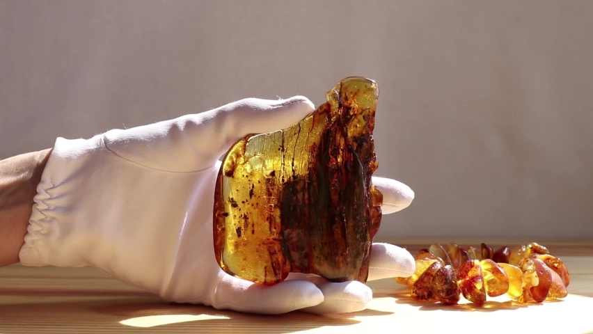 A woman's gloved hand shows a large piece of Baltic orange amber in the sunlight.  Ancient amber stone is healing, protection, luck and strength. Royalty-Free Stock Footage #1070743279