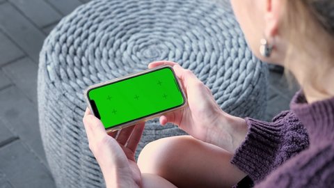 USA - April 13 2021: Woman using smartphone iPhone 12 horizontal green screen. Mock-up for tracking or watching content. Blank digital phone in hand of girl. 