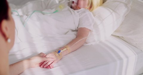mother holding a hand of acutely sick kid with intravenous fluid therapy and oxygen mask for lung ventilation