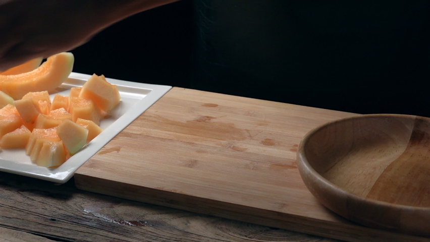 man cutting Melon into pieces on a wooden board