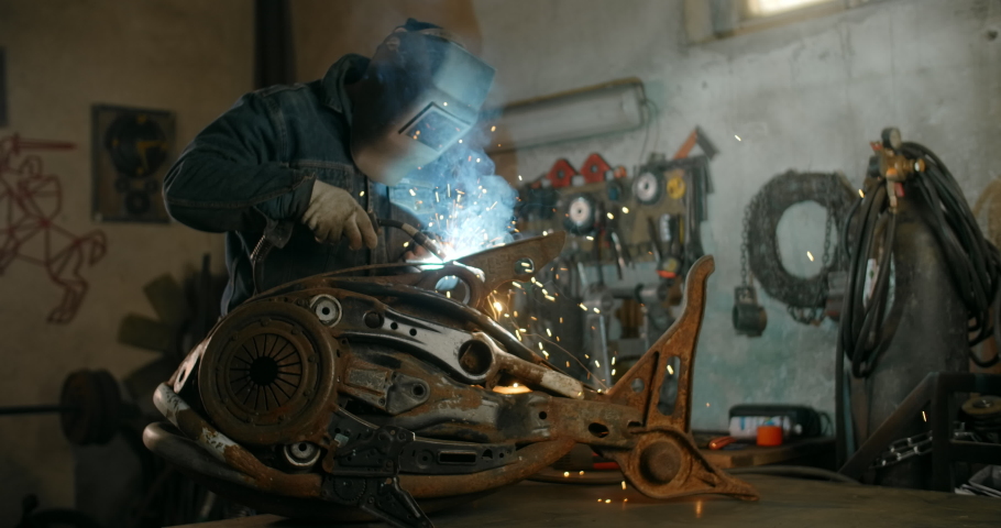 Locksmith welds the decorative metal steampunk fish sculpture with a lot of sparks and flashes in slow motion, metalwork at workshop, 4k 60p Prores HQ