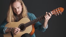 Young long haired male musician playing on acoustic guitar and singing over black background