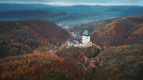 Aerial view of the famous Karlstein Castle - a beautiful medieval castle standing on the hill, overlooking the dense forest. Villages are scattered through the valley below. A tilt-shift video.