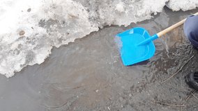 4K video, child with pleasure plays with a shovel in a muddy puddle with snow and ice, dressed in rubber boots and a jacket, early spring in the yard