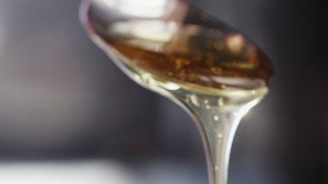 Close up shot of golden honey pouring from a silver spoon