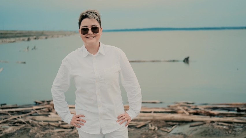 Beautiful girl with a short haircut in glasses is dancing on the shore looking at the camera. LGBT