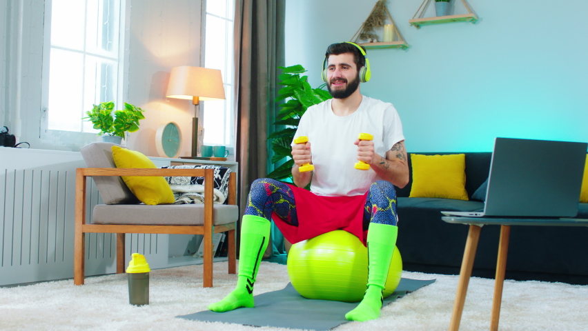 A man working on his biceps is very happy with himself, he is smiling a lot while using the yellow weights and working out on a ball