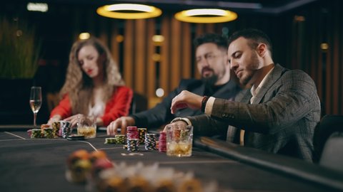 Two bearded men and young woman are looking intently at their poker playing cards make bets gambiling in a casino. Entertainment industry and luxury lifestyle. Concept of casino gambling and poker.