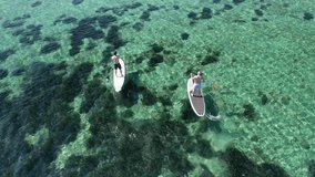 Aerial drone video of friends exercising sup board or Stand Up Paddle board in emerald exotic shallow bay