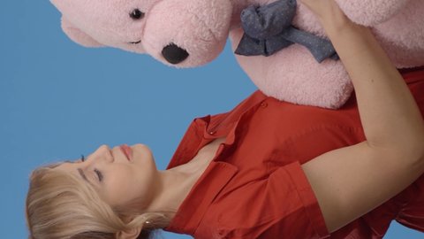 Young woman talking, hugging and kissing with a big teddy bear.Indoor studio shot isolated on blue background.Video for the vertical story.