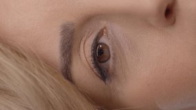 Very close-up of a young woman's surprised eyes.Studio shot isolated on blue background.Video for the vertical story.