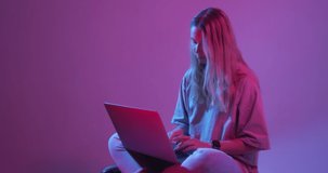 4k video of modern young girl blogger with laptop, typing on computer. Colored Neon light and background