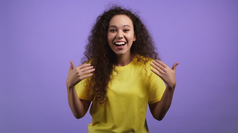 Young woman showing - Hey you, come here. Pretty girl in yellow wear ask join her,beckons with inviting hand hugs gesture.She is looking playful flirtatious, inviting to come.Violet studio background.
