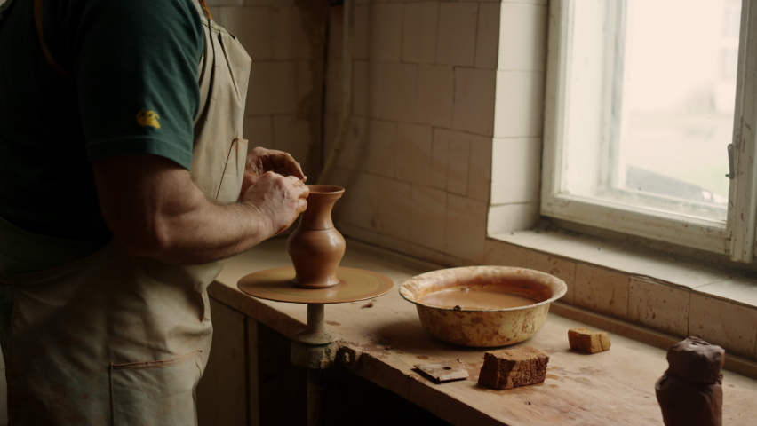 Closeup senior man sculpting jar in workshop. Elderly artist modeling jar in studio on potters wheel. Serious ceramist making clay product in pottery in slow motion. Royalty-Free Stock Footage #1070777887