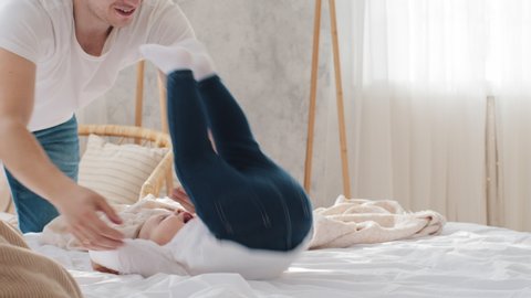Caring young father dad playing game with little daughter having fun at home with beloved adorable child holding kid toddler on bed, baby does somersault turns over acrobatic exercise looks at camera
