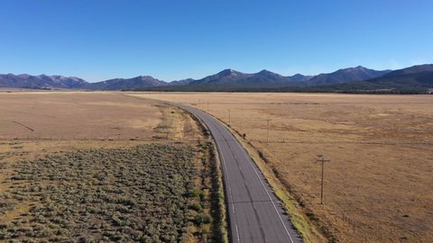 Drone camera gliding over a peaceful open road landscape with the Rocky Mountains in the distance.  