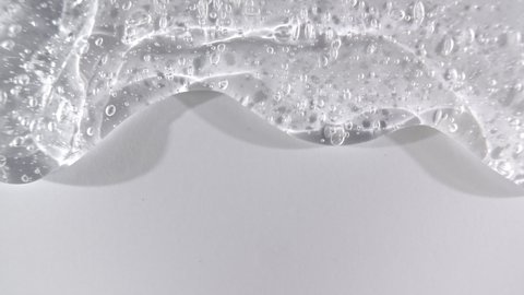 Transparent cosmetic gel fluid flowing down on a white surface. Macro Shot