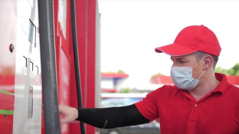 Caucasian man employee wearing a face mask refueling to car with gasoline holding filling nozzle at the gas station pump, Petrol station service, Coronavirus pandemic.