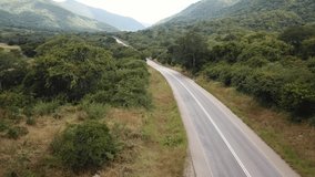 Aerial View of the Green Plains in Mountains and Trafic Road, Tanzania, Africa. The the Green Hills Mountains in East Africa. Beautiful Lush Savanna Nature Landscape. 4K Video. Camera Moves Forward