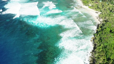 Aerial reveal of coast line of Siargao Island, Philippines. Long waves, turquoise water, reef and palm trees