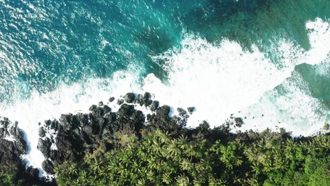 Aerial top down view of coast line of Siargao Island, Philippines. White waves crushing over rocks, turquoise water and palm trees. Peaceful and relaxing parallel layout