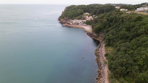 Aerial circling shot of stony famous Babbacombe Beach with green cliffs and Torquay Town on top of mountain.
