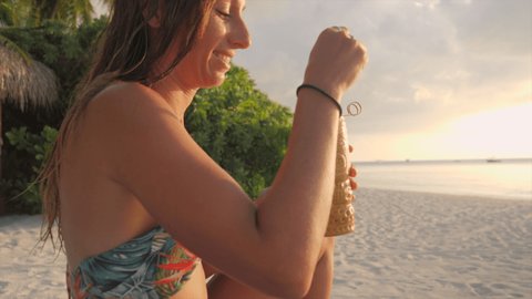 Young female enjoys sunset with a cocktail from tropical beach bar. Woman on vacation having a drink on the beach 