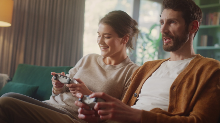 Happy Couple Sitting on the Sofa Playing Video Games, Using Controllers. Competitive Girlfriend and Boyfriend in Love have Fun Playing in Online Video Games at Home Together | Shutterstock HD Video #1070800768