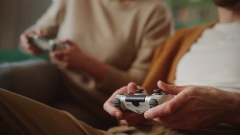 Happy Couple Sitting on the Sofa Playing Video Games, Using Controllers. Competitive Girlfriend and Boyfriend in Love have Fun Playing in Online Video Games at Home Together. Close-up Focus on Hands