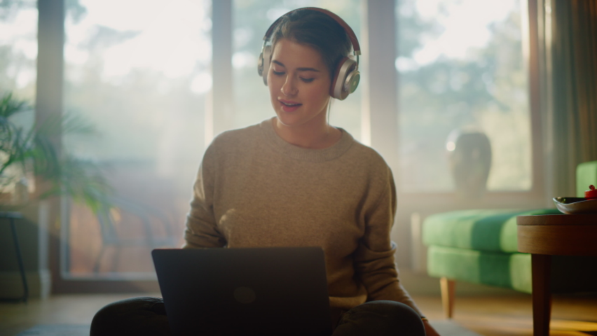 Young Woman Using Laptop at Home, Does Remote Work, Listens Music through Headphones. Beautiful Smiling Girl Sitting on the Floor Enjoys Music, Dances a Bit, Brainstorms Creative Project | Shutterstock HD Video #1070800954