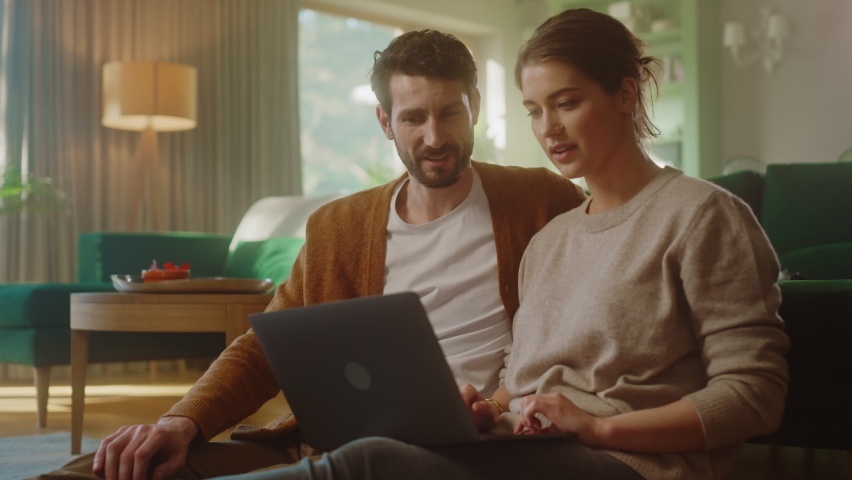 Couple Use Laptop Computer, Do High-Five in Celebration, while Sitting in the Cozy Living Room. Successful Boyfriend and Girlfriend Talk, Shop on Internet, Choose Product to Order Online. Slow Motion Royalty-Free Stock Footage #1070801008