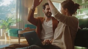 Couple Use Laptop Computer, Do High-Five in Celebration, while Sitting in the Cozy Living Room. Successful Boyfriend and Girlfriend Talk, Shop on Internet, Choose Product to Order Online. Slow Motion - Powered by Shutterstock - Get 15% off with code: PIKWIZARD15
