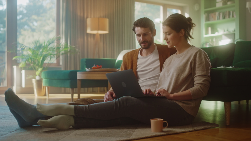 Couple Use Laptop Computer, Do High-Five in Celebration, while Sitting on the Living Floor room of their Apartment. Boyfriend and Girlfriend Talk, Shop on Internet, Choose Product to Order Online | Shutterstock HD Video #1070801011